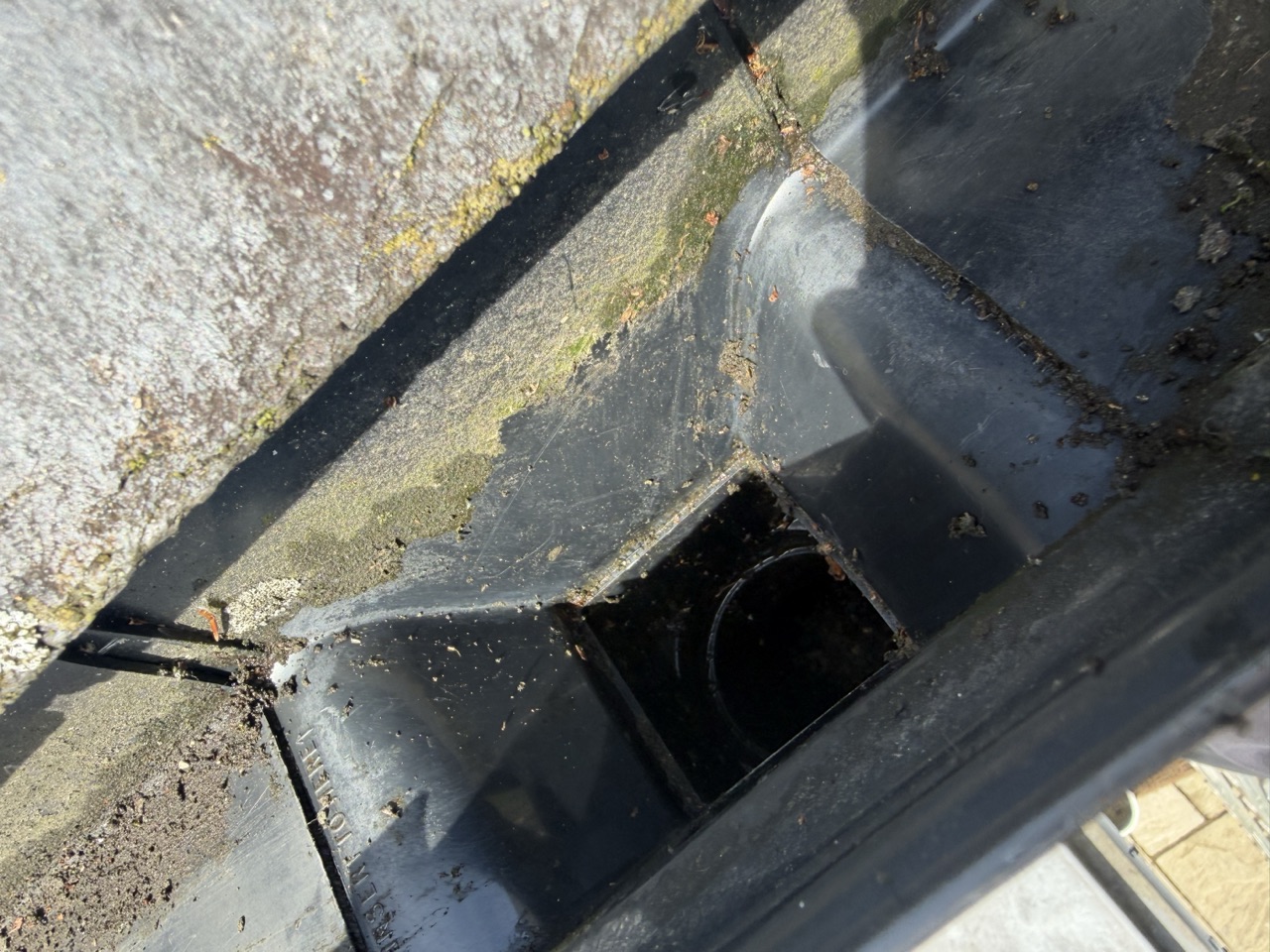 A blocked gutter outlet packed with moss and debris